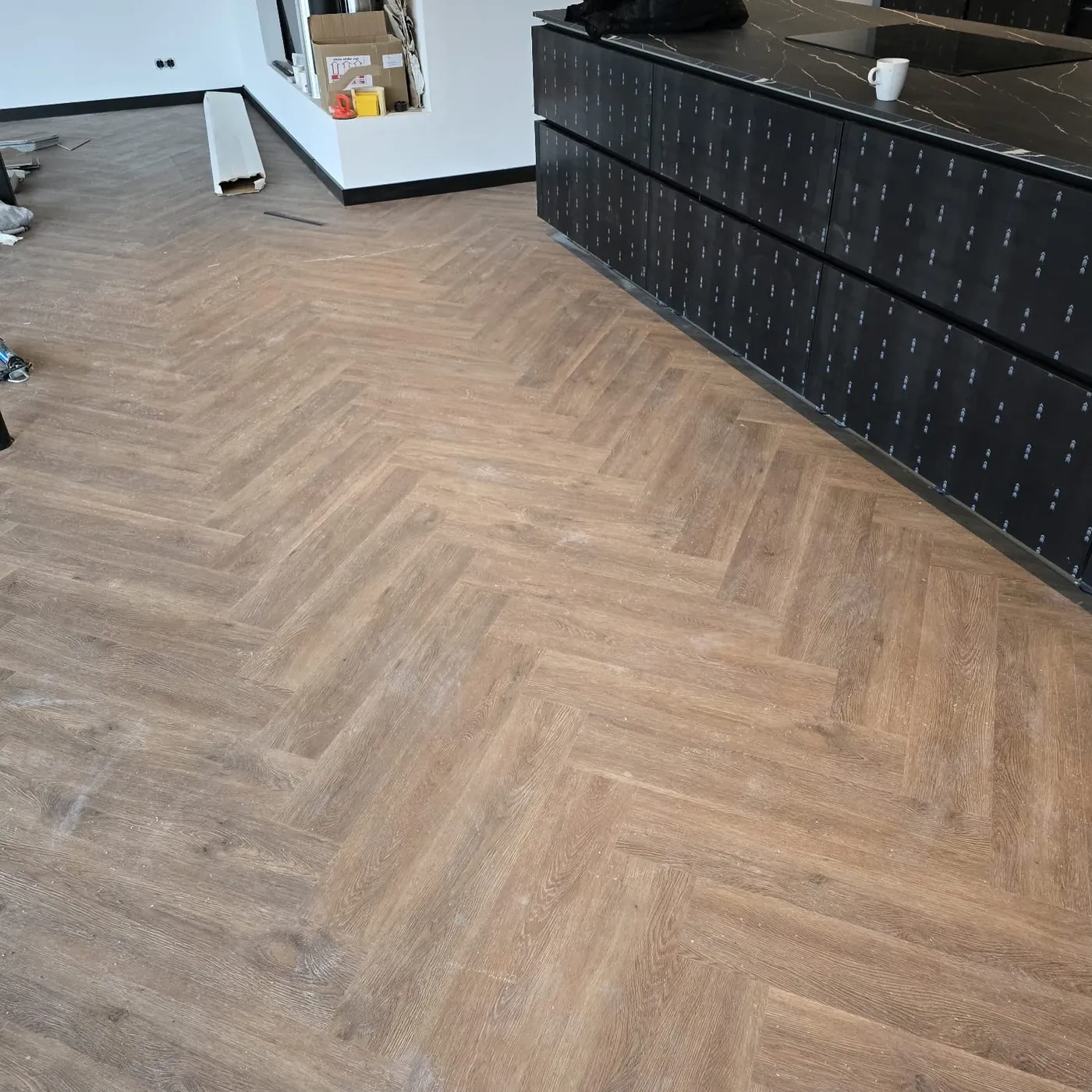 Visgraatvloer naast een zwart keukenblok