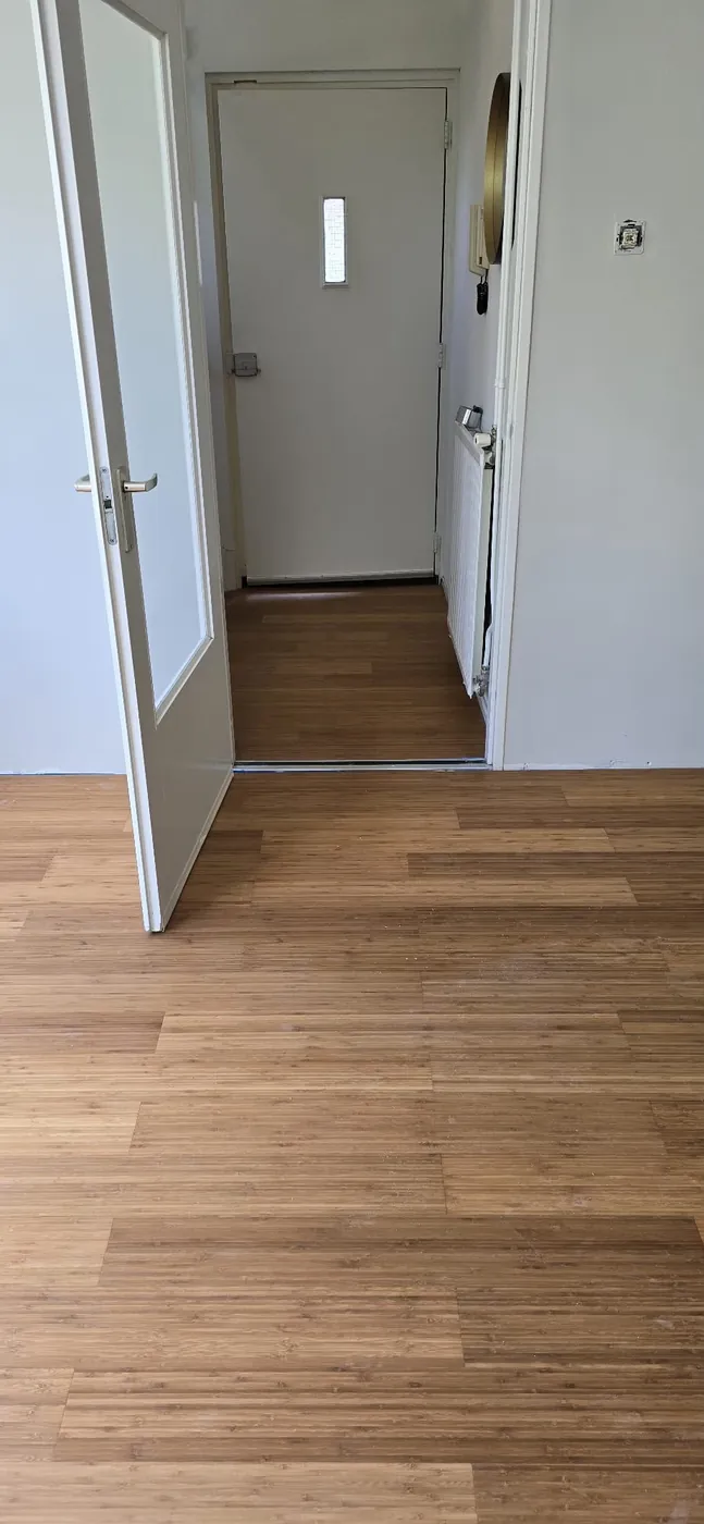 Gang met een warme eikenkleurige vloer en een open deur